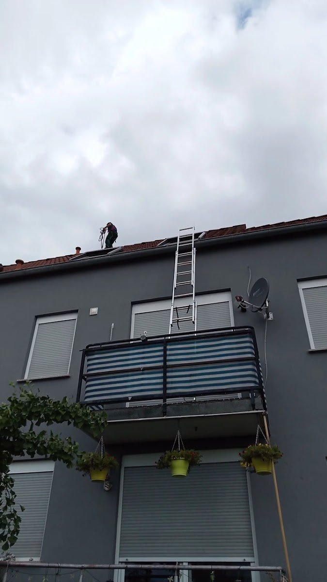 Mehrfamilienhaus mit angelehnter Leiter, ein Mitarbeiter arbeitet auf dem Dach