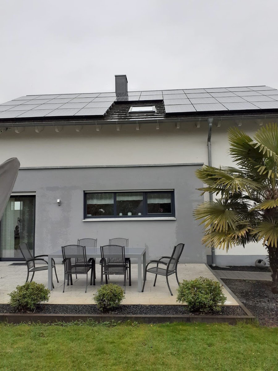 Rückseite eines hellen Wohnhauses mit Terrasse und Gartenmöbeln